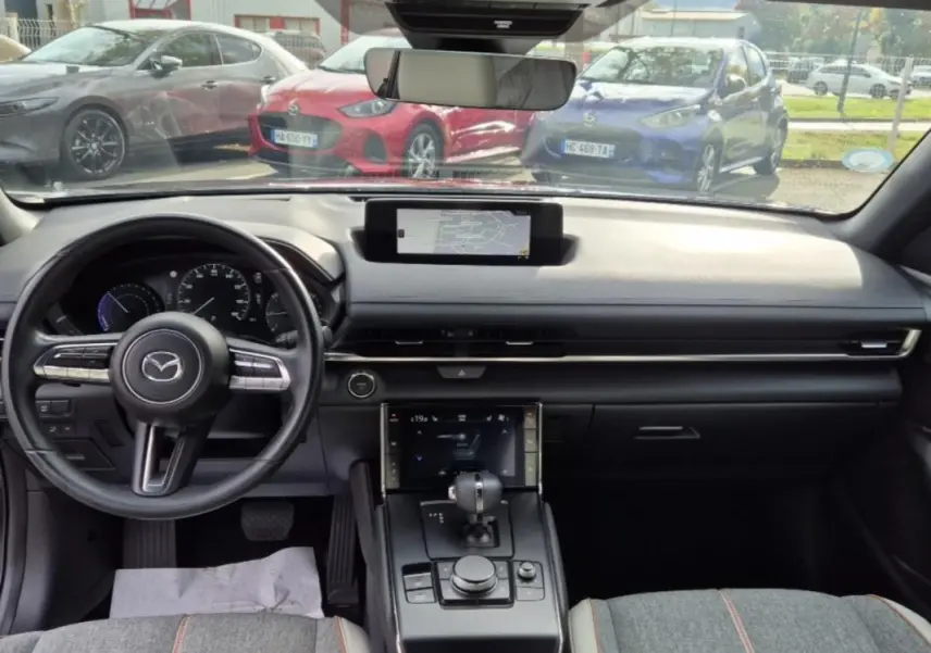 Intérieur de la Mazda MX-30 2021, vue de face sur le tableau de bord noir avec écran central et volant multifonction.