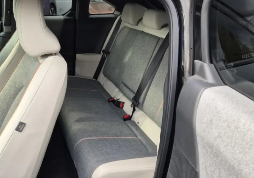 Vue intérieure arrière droite du Mazda MX-30 2021, sellerie moderne gris clair avec surpiqûres orange et ceintures noires.