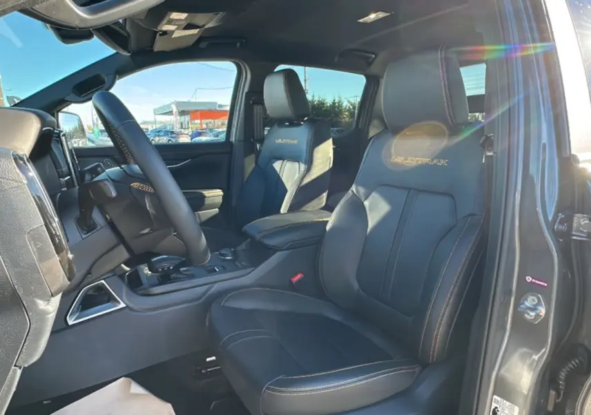 Intérieur du Ford Ranger Wildtrak gris carbone, vue côté conducteur sur sièges cuir noirs avec logo Wildtrak brodé.