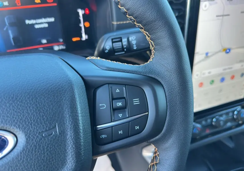 Gros plan sur le volant cuir noir avec surpiqûres jaunes du Ford Ranger Wildtrak Plus 2025 et son écran tactile GPS.