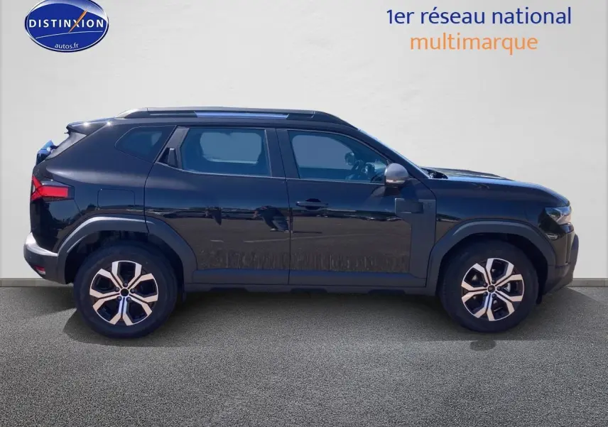 Profil latéral droit du Dacia Duster noir 2025 avec jantes alu et barres de toit visibles sur fond neutre.