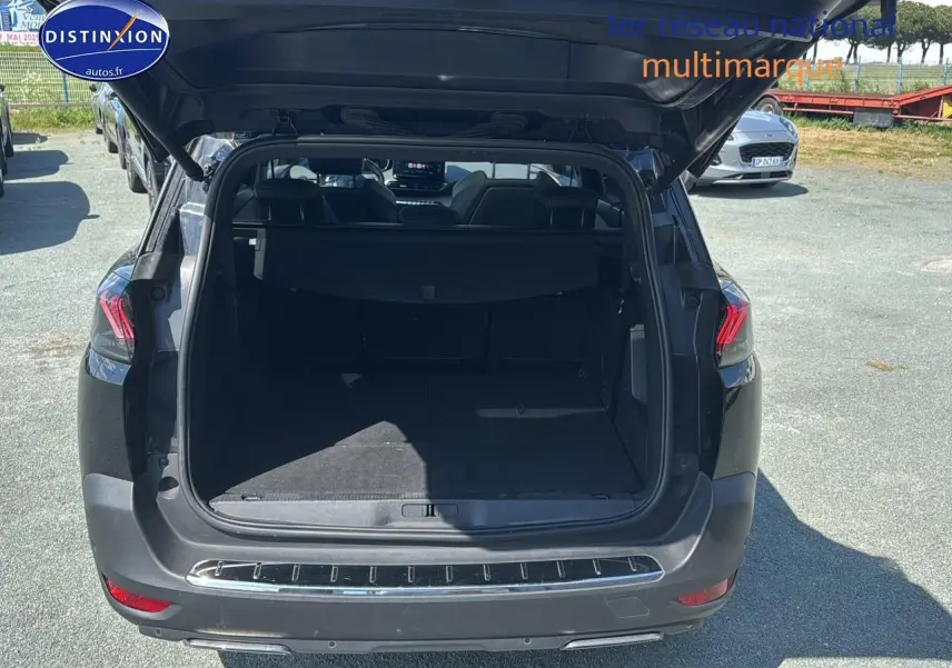 Coffre ouvert vu de l'arrière d'un Peugeot 5008 noir métal, avec intérieur spacieux et sièges arrière visibles.