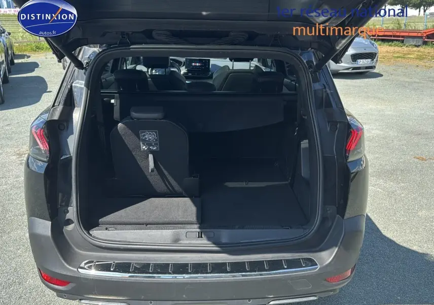 Coffre ouvert vu de l'arrière d'un Peugeot 5008 noir métal 2022 avec banquette arrière partiellement rabattue.