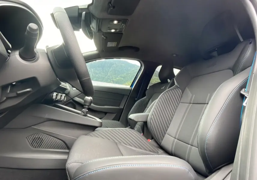 Vue intérieure côté conducteur de la Renault Clio V TCE 90 Esprit Alpine 2025 avec sièges sport noirs et surpiqûres bleues.