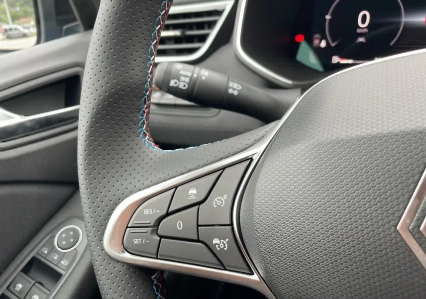 Gros plan sur le volant perforé de la Renault Clio V TCE 90 Esprit Alpine 2025, avec surpiqûres tricolores et commandes intégrées.