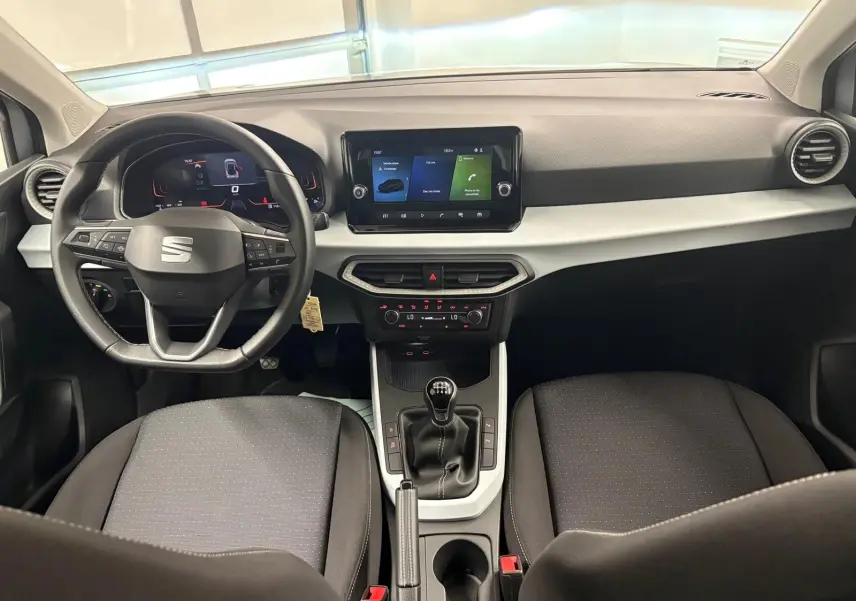 Intérieur avant du SEAT Arona 2024 avec tableau de bord moderne, écran tactile et boîte manuelle, sièges noirs.