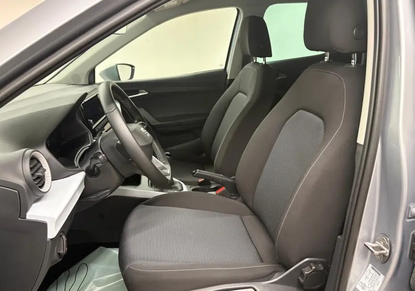 Vue intérieure côté conducteur du SEAT ARONA gris urbain 2024, sièges en tissu noir et tableau de bord moderne.