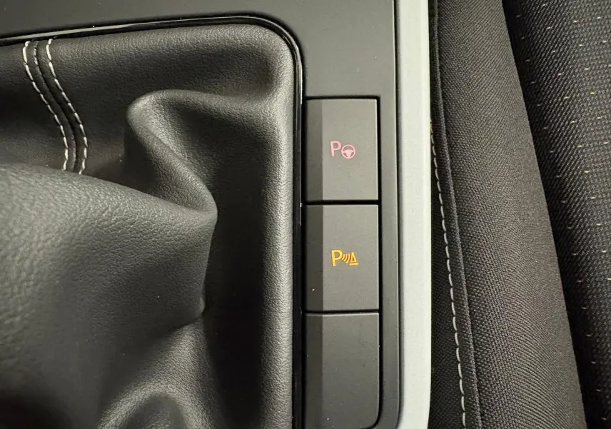 Gros plan sur la console centrale du SEAT Arona 2024 montrant le soufflet de levier de vitesses et les boutons d'aide au stationnement.