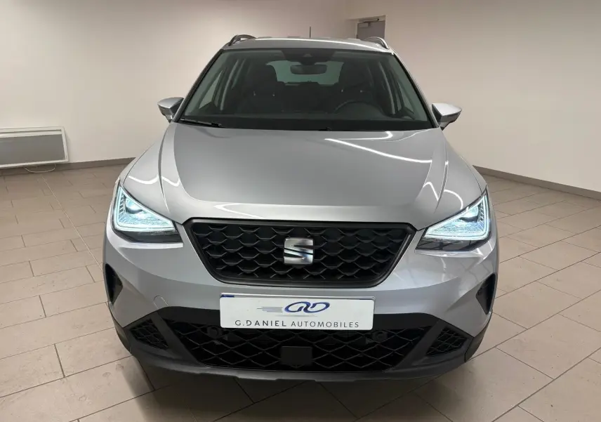 Vue frontale d'un SEAT Arona 2024 gris urbain avec phares LED allumés et calandre noire en intérieur showroom.