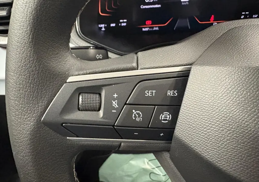 Gros plan sur les commandes du volant gauche du SEAT Arona 2024 gris urbain, avec régulateur de vitesse et volume.