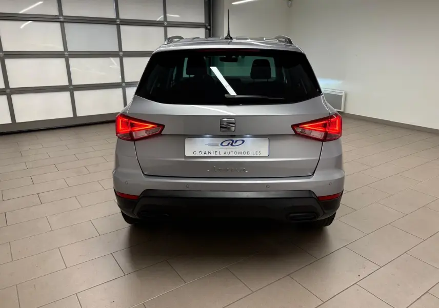 Vue arrière d'un SEAT Arona 2024 gris urbain avec vitres surteintées et feux arrière allumés dans un garage.