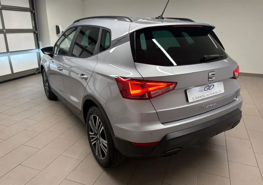 SEAT Arona gris urbain en 3/4 arrière droit, vitres arrière surteintées et feux arrière allumés en intérieur showroom.