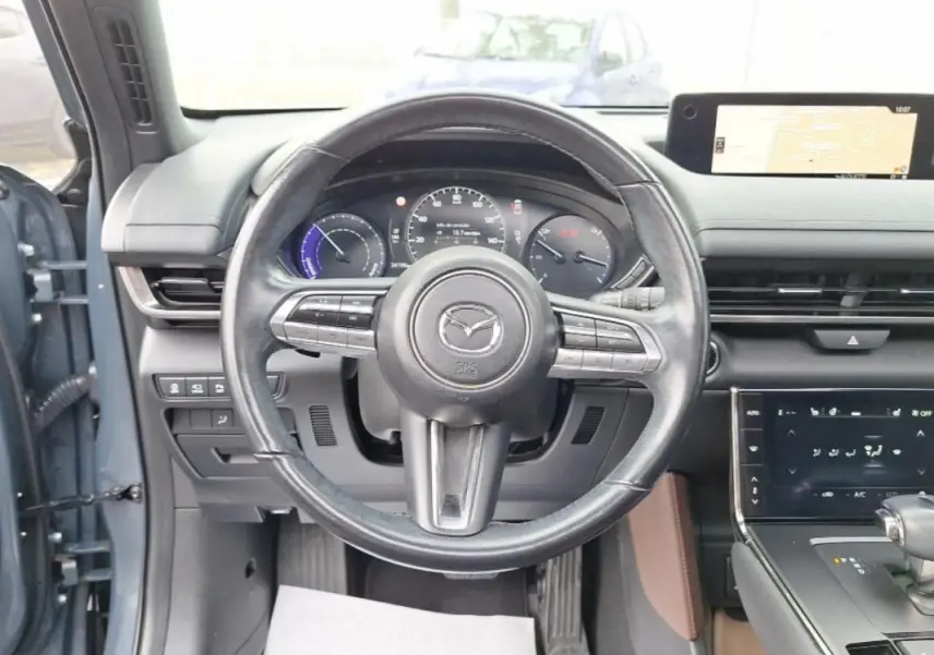 Vue intérieure centrée sur le volant noir du Mazda MX-30 gris, avec tableau de bord numérique et écran tactile visible.