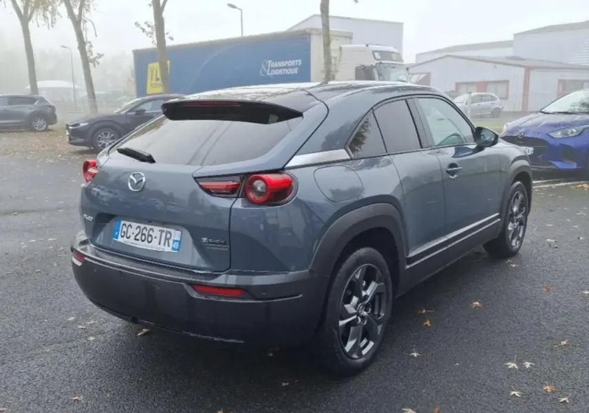 Vue 3/4 arrière droite d'un Mazda MX-30 gris électrique 2021 avec feux arrière ronds et jantes foncées.