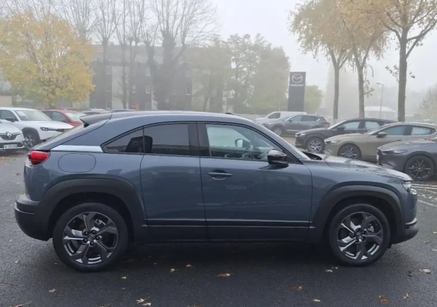 Vue de profil côté gauche d’un Mazda MX-30 gris électrique 2021 avec jantes spécifiques et toit noir contrasté.