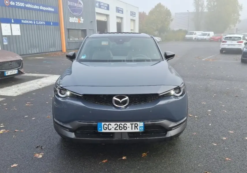 Vue frontale d'un Mazda MX-30 gris électrique 2021, avec calandre noire et phares LED allumés.