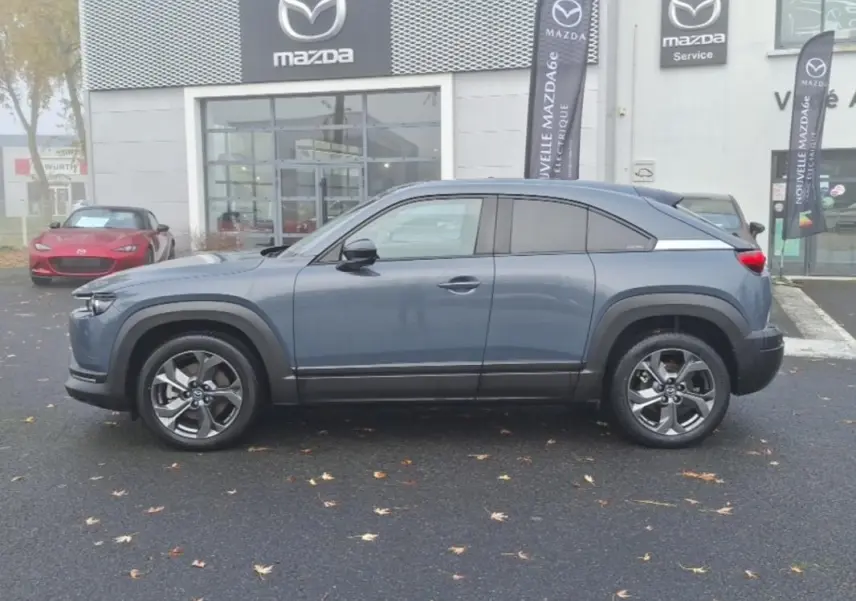 Vue de profil côté gauche d'un Mazda MX-30 gris électrique 2021 devant une concession Mazda.