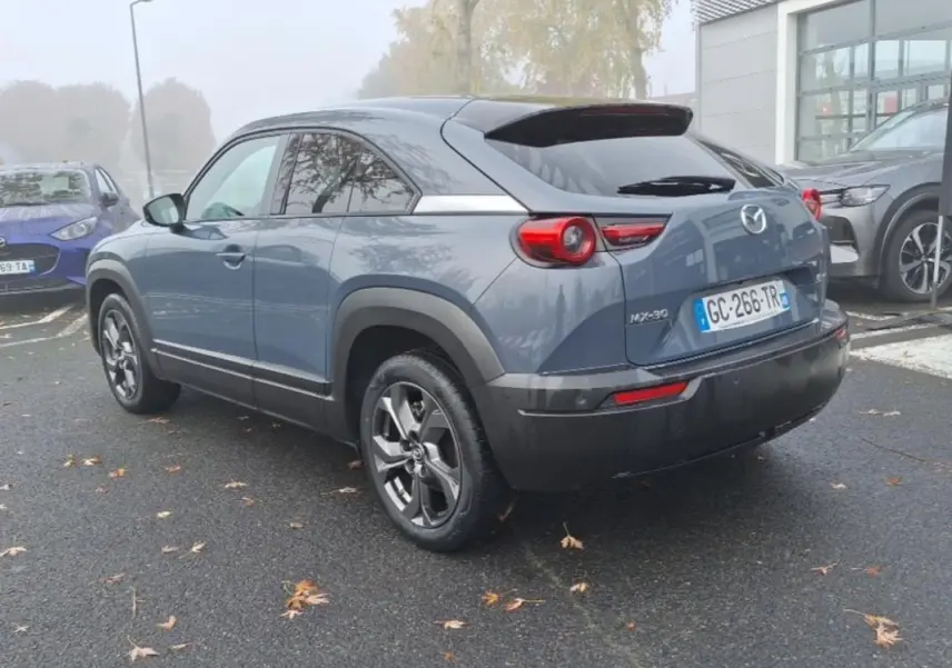 Vue 3/4 arrière droite d'un Mazda MX-30 gris électrique 2021 avec jantes distinctives et feux ronds arrière.