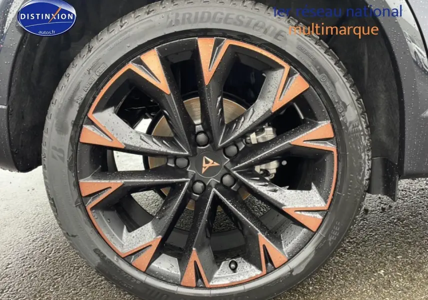 Gros plan sur la jante noire et cuivre du CUPRA Formentor gris graphene, avec pneu Bridgestone sous la pluie.