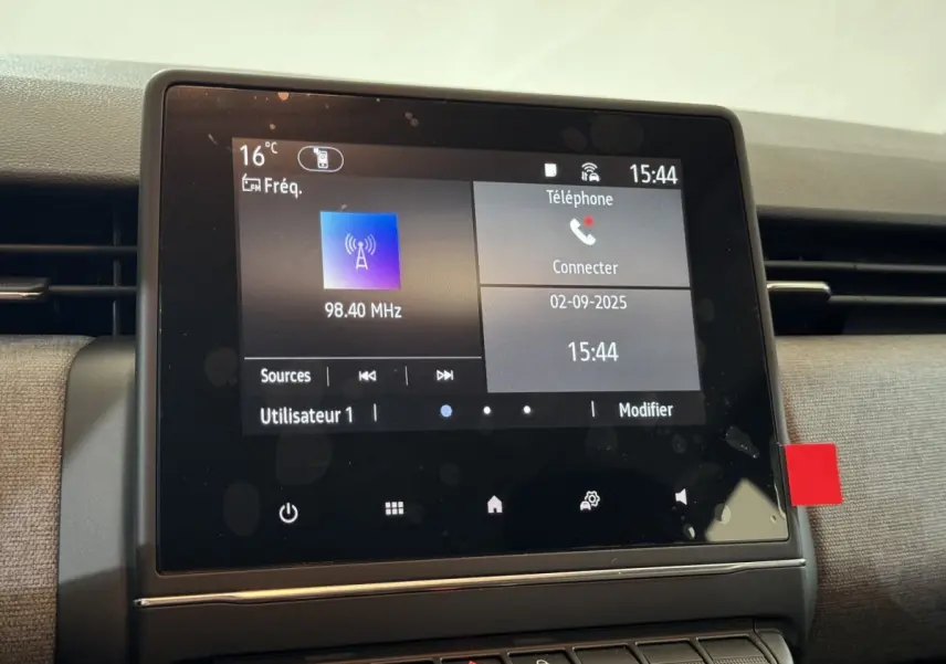 Écran tactile central de la Renault Clio gris clair, affichant la radio et les options téléphone, vue de face rapprochée.