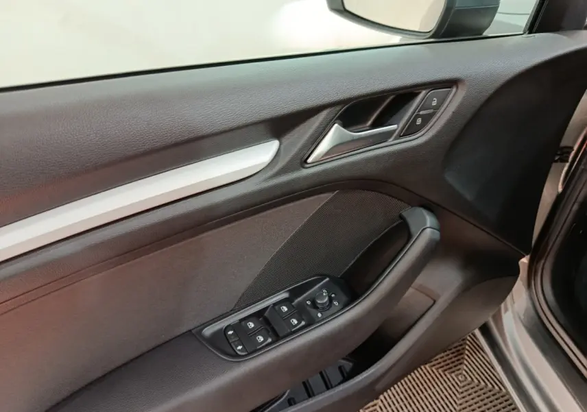 Vue intérieure du panneau de porte avant côté conducteur de l'Audi A3 gris foncé, avec commandes électriques et verrouillage.