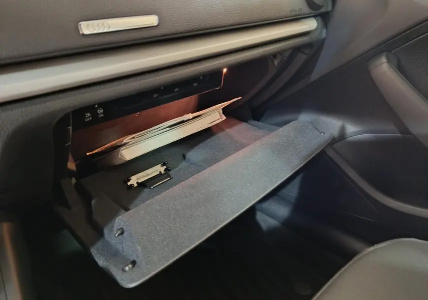 Gros plan sur la boîte à gants ouverte côté passager de l’Audi A3 35 TDI 2020 avec intérieur noir et éclairage intérieur.