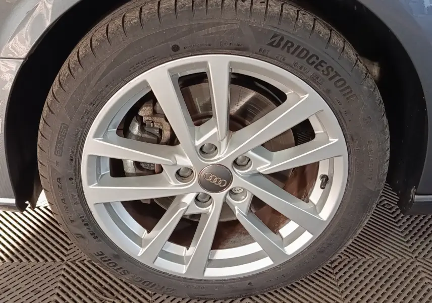 Gros plan sur la roue avant droite d'une Audi A3 gris foncé, jante alliage à plusieurs branches fines.