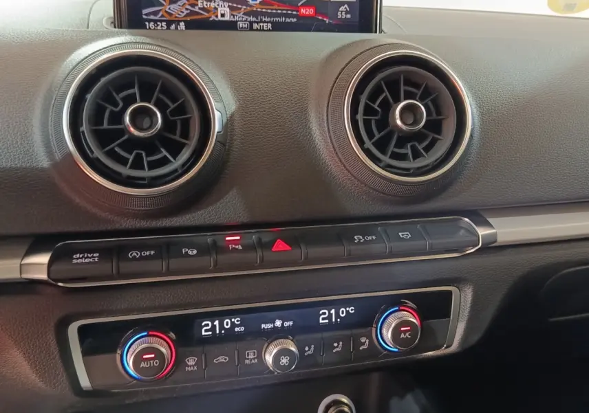 Vue rapprochée du tableau de bord de l’Audi A3 35 TDI 2020, montrant les aérateurs ronds et la climatisation digitale à 21°C.