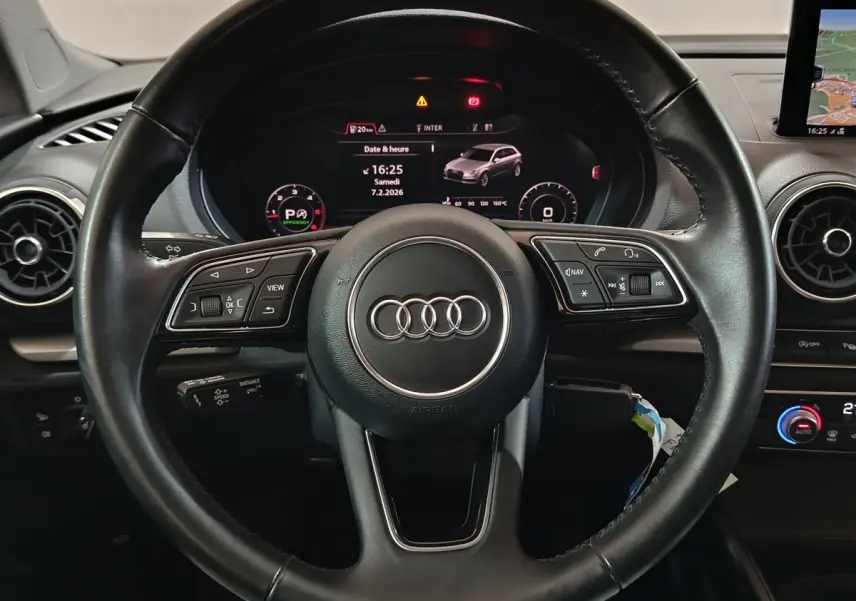 Vue intérieure centrée sur le volant cuir noir de l'Audi A3 35 TDI avec tableau de bord numérique et écran navigation.