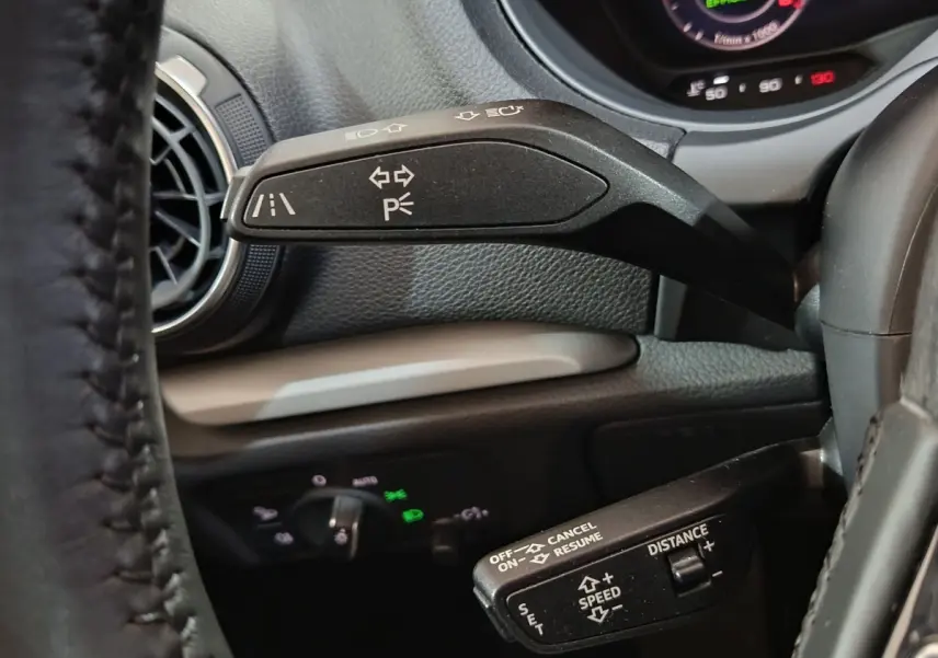 Gros plan intérieur sur la commande de clignotants et régulateur de vitesse d’un Audi A3 gris foncé, tableau de bord en arrière-plan.