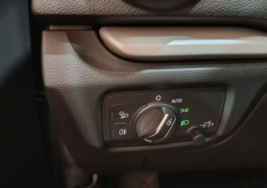 Gros plan sur le bouton de commande des phares avec réglage automatique dans l’habitacle gris foncé de l’Audi A3 35 TDI.