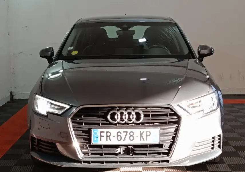 Vue de face d'une Audi A3 gris foncé avec phares allumés et calandre hexagonale distinctive.