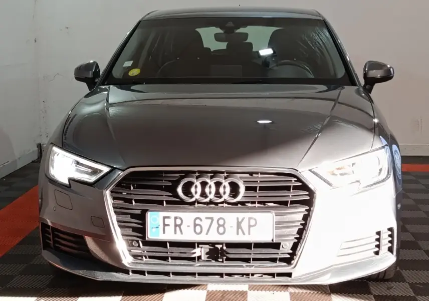 Vue frontale d'une Audi A3 gris foncé 35 TDI 150 S tronic avec phares LED allumés et calandre distinctive.