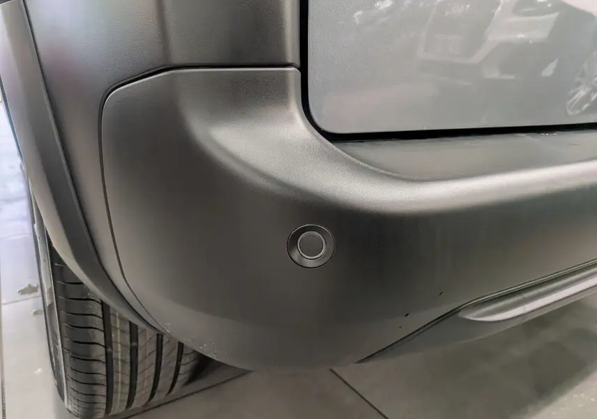 Gros plan sur le pare-chocs arrière gris acier du Peugeot Rifter 2025, avec capteur de stationnement visible.