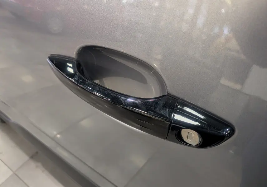 Poignée de porte noire en gros plan sur la portière côté gauche d'un Peugeot Rifter gris acier 2025.