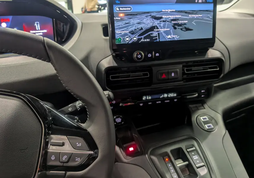 Vue intérieure côté conducteur du Peugeot Rifter 2025, montrant le volant, l'écran tactile central avec navigation et la console centrale moderne.