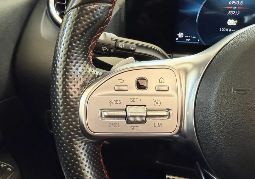 Gros plan sur le volant cuir perforé noir avec commandes argentées du Mercedes GLA 250 e AMG Line, affichage digital en arrière-plan.