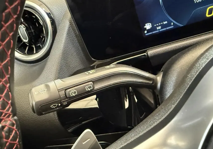 Gros plan sur la manette d'essuie-glace à gauche du volant avec volant cuir noir sur fond de tableau de bord numérique.