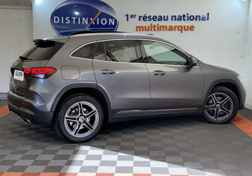 Vue de profil côté droit d’un Mercedes GLA 250 e AMG Line gris clair dans un showroom avec logo Distinxion en arrière-plan.