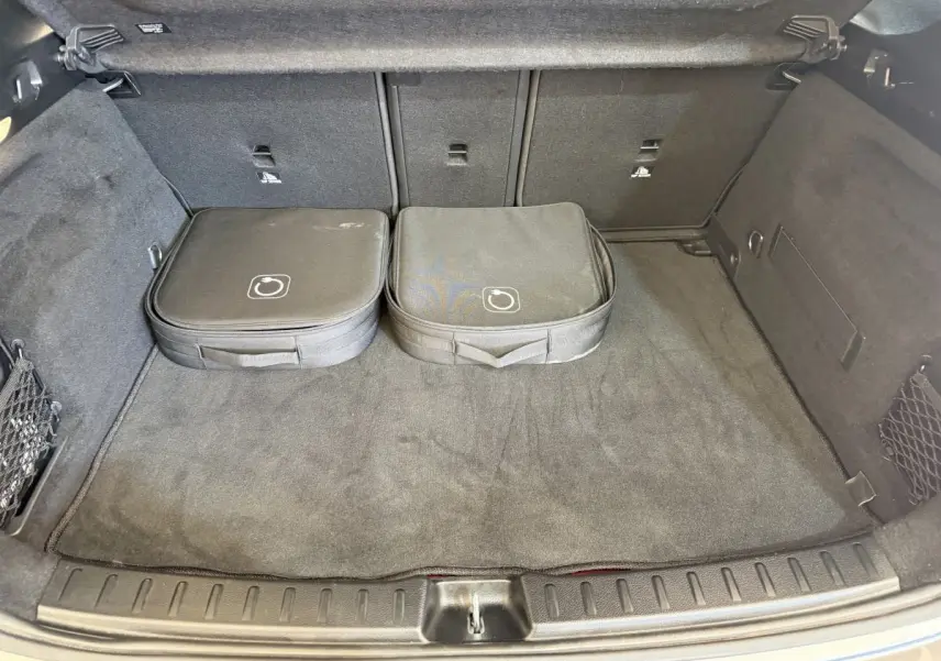 Coffre ouvert d’une Mercedes GLA 250 e AMG Line gris clair, vue intérieure avec deux sacs de rangement noirs.