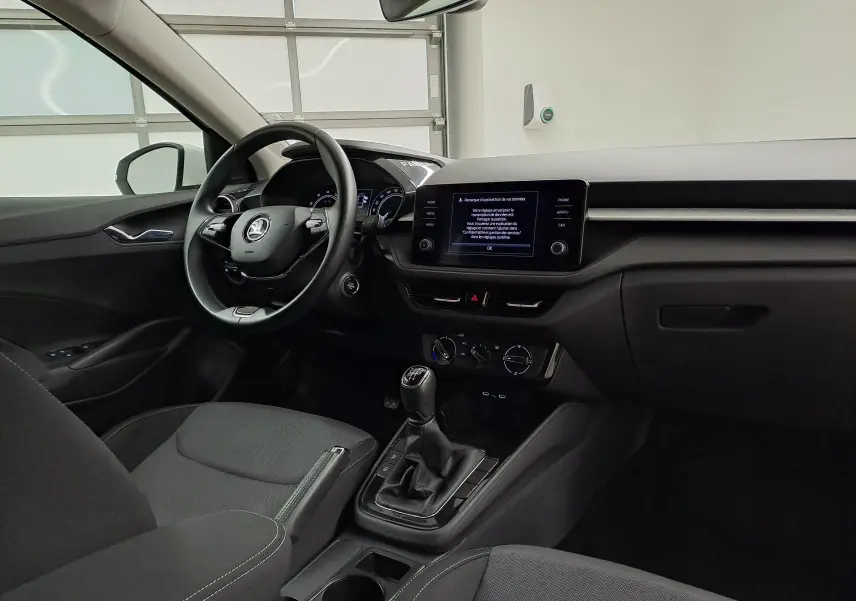 Vue intérieure côté conducteur de la Skoda Fabia 2023 blanche, avec tableau de bord moderne et boîte manuelle visible.