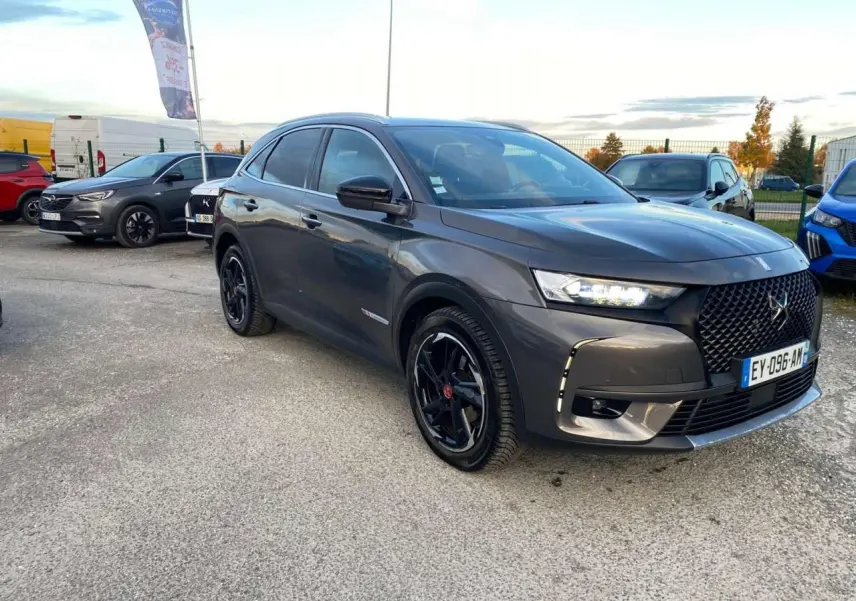 DS7 Crossback gris foncé en 3/4 avant droit, avec calandre noire et jantes noires brillantes sur parking extérieur.