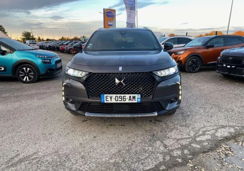 Vue frontale d'un DS7 Crossback gris foncé 2018 avec calandre noire et feux LED allumés sur un parking.