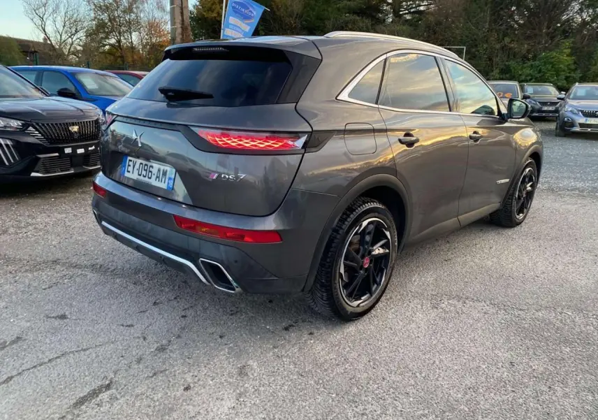 DS7 Crossback gris foncé en 3/4 arrière droit, avec feux arrière allumés et jantes noires distinctives.