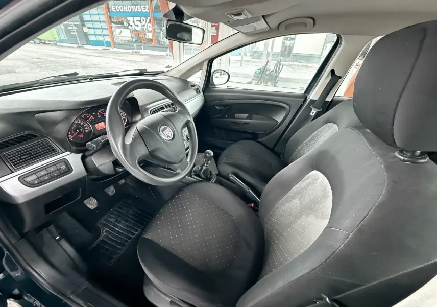 Intérieur de la Fiat Punto 1.2 i 65 de 2009, vue côté conducteur, sièges noirs et tableau de bord simple.