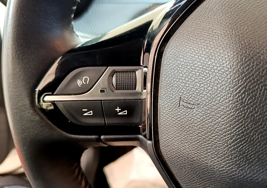 Gros plan sur les commandes gauche du volant cuir noir du Peugeot 2008 blanc, version 1.5 BlueHDi 2021.