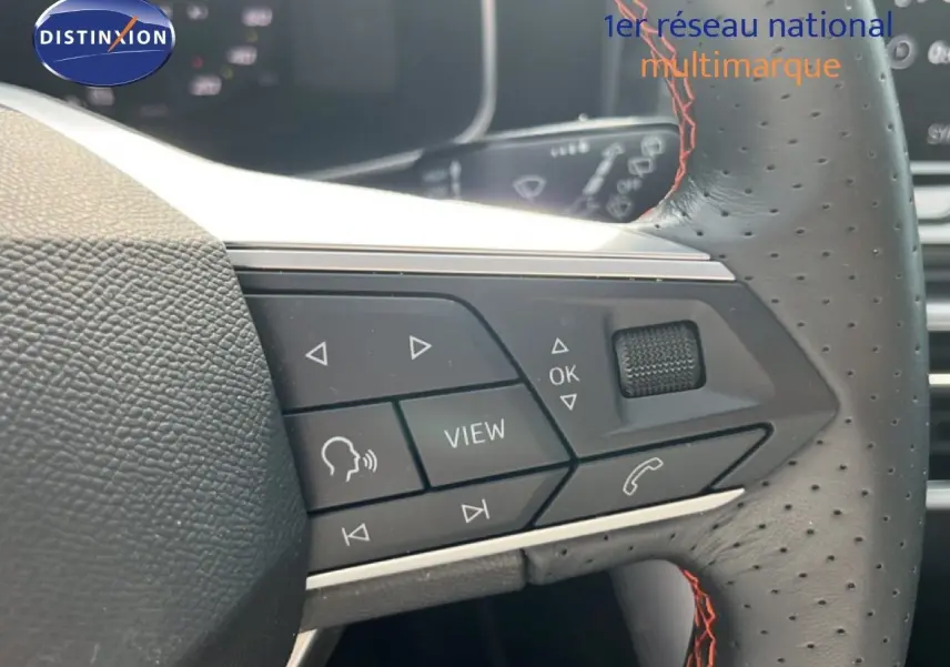 Gros plan sur le volant perforé avec surpiqûres rouges du SEAT LEON ST gris magnétique, montrant les commandes multifonctions.
