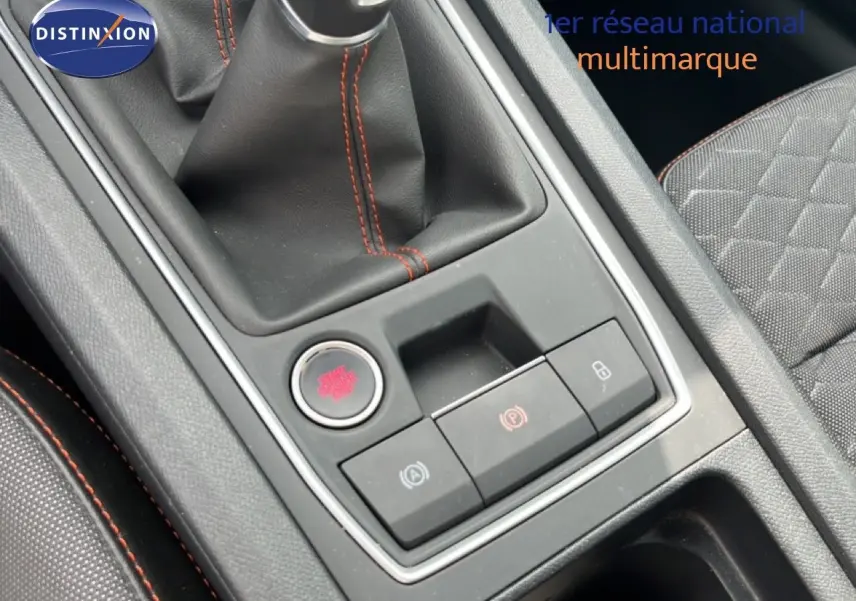 Gros plan sur la console centrale avec levier de vitesse et boutons de contrôle, intérieur tissu gris avec surpiqûres rouges.