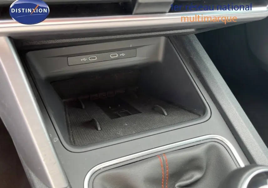 Gros plan sur la console centrale d’une SEAT Leon ST 2025, montrant les ports USB et le soufflet de levier de vitesses noir avec surpiqûres rouges.