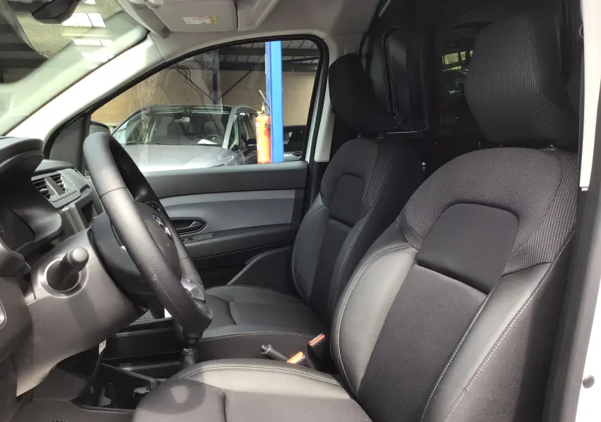 Vue intérieure côté conducteur du Renault Express Van blanc 2024, sièges noirs avec cloison séparatrice métallique.